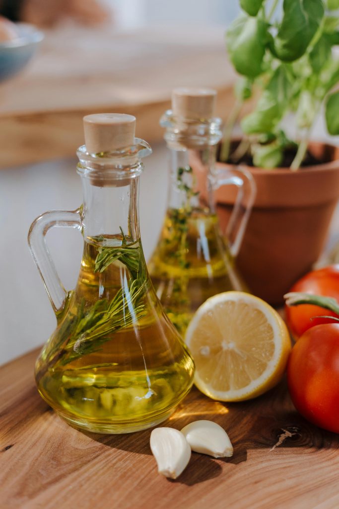 Bottles of olive oil with herbs, tomatoes, and lemon for Mediterranean cuisine.