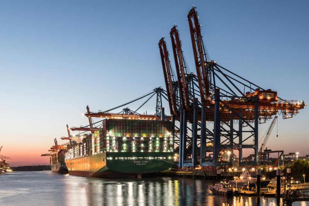 A large container ship at the Hamburg port with cranes during twilight, showcasing global trade.